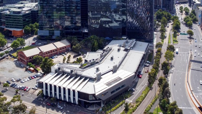 A high-angle drone shot of the angular, modern building, nestled among taller glass skyscrapers