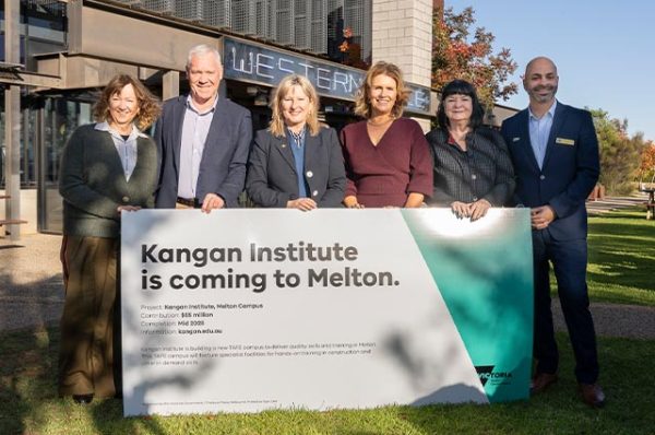 A group of six people standing outdoors holding a large sign that announces, "Kangan Institute is coming to Melton" with details about the new campus project.